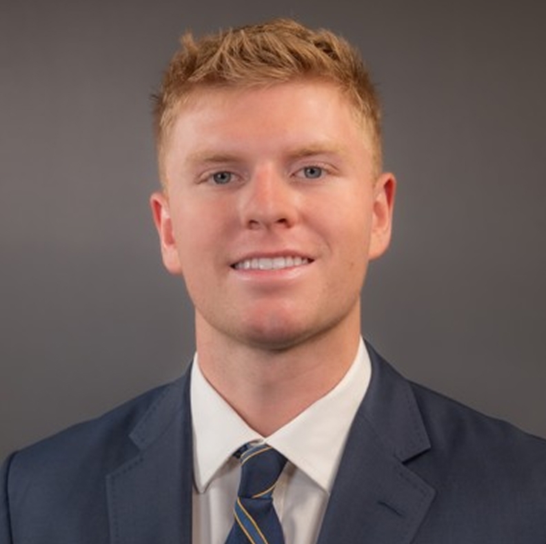 Tye Wydner in a suit with a white shirt and blue striped tie, smiling against a plain background.