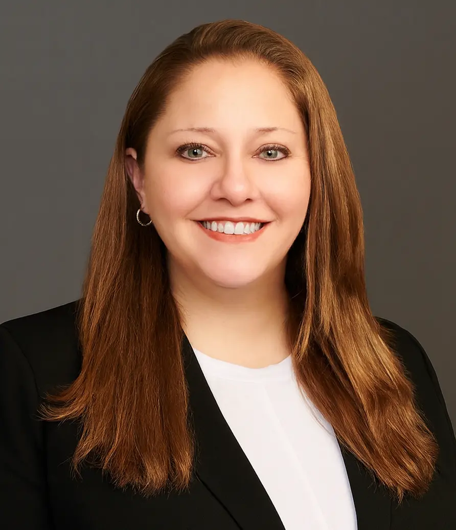 Christine Janaske wearing a black blazer and white top, smiling against a gray background.