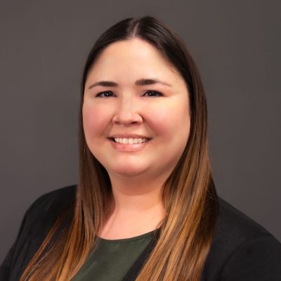 Smiling Human Resources Coordinator in a black blazer and green top against a plain background.