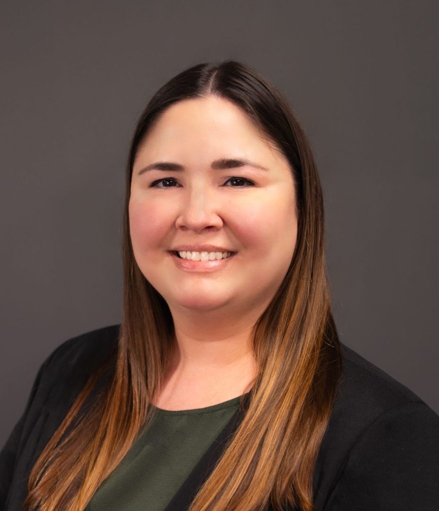 Smiling Human Resources Coordinator in a black blazer and green top against a plain background.