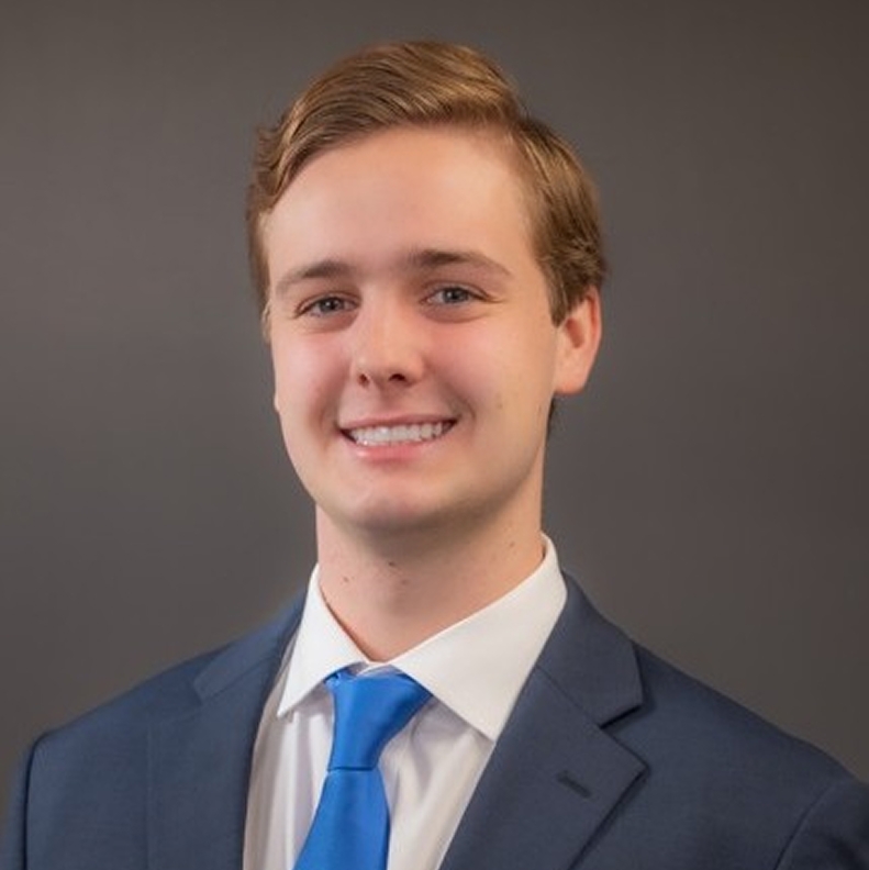 Grant Barlow in a blue suit and tie, smiling against a plain gray background.