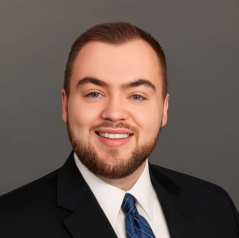 Jack Loesch smiling, wearing a suit and blue tie against a gray background.