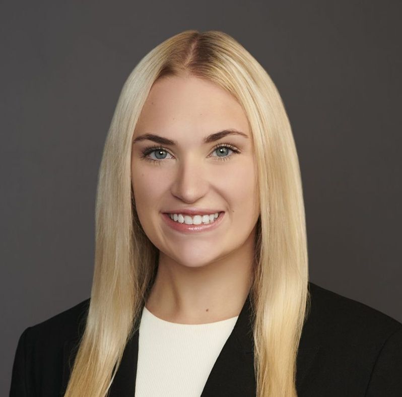 Elise Wente smiling, wearing a black blazer and white top, with long blonde hair against a gray background.