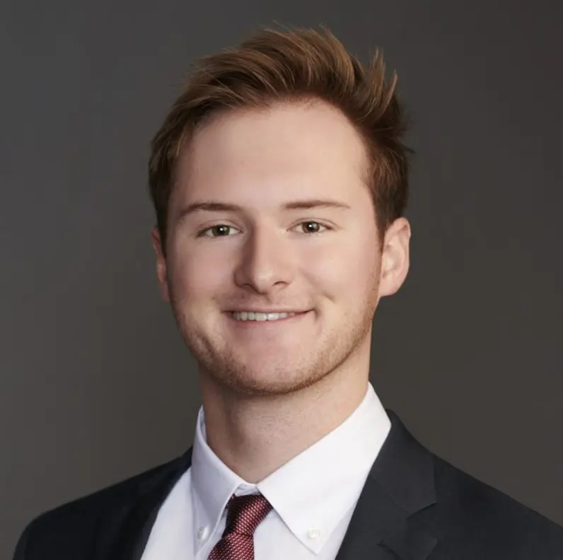 Smiling man in a suit and tie against a gray background.