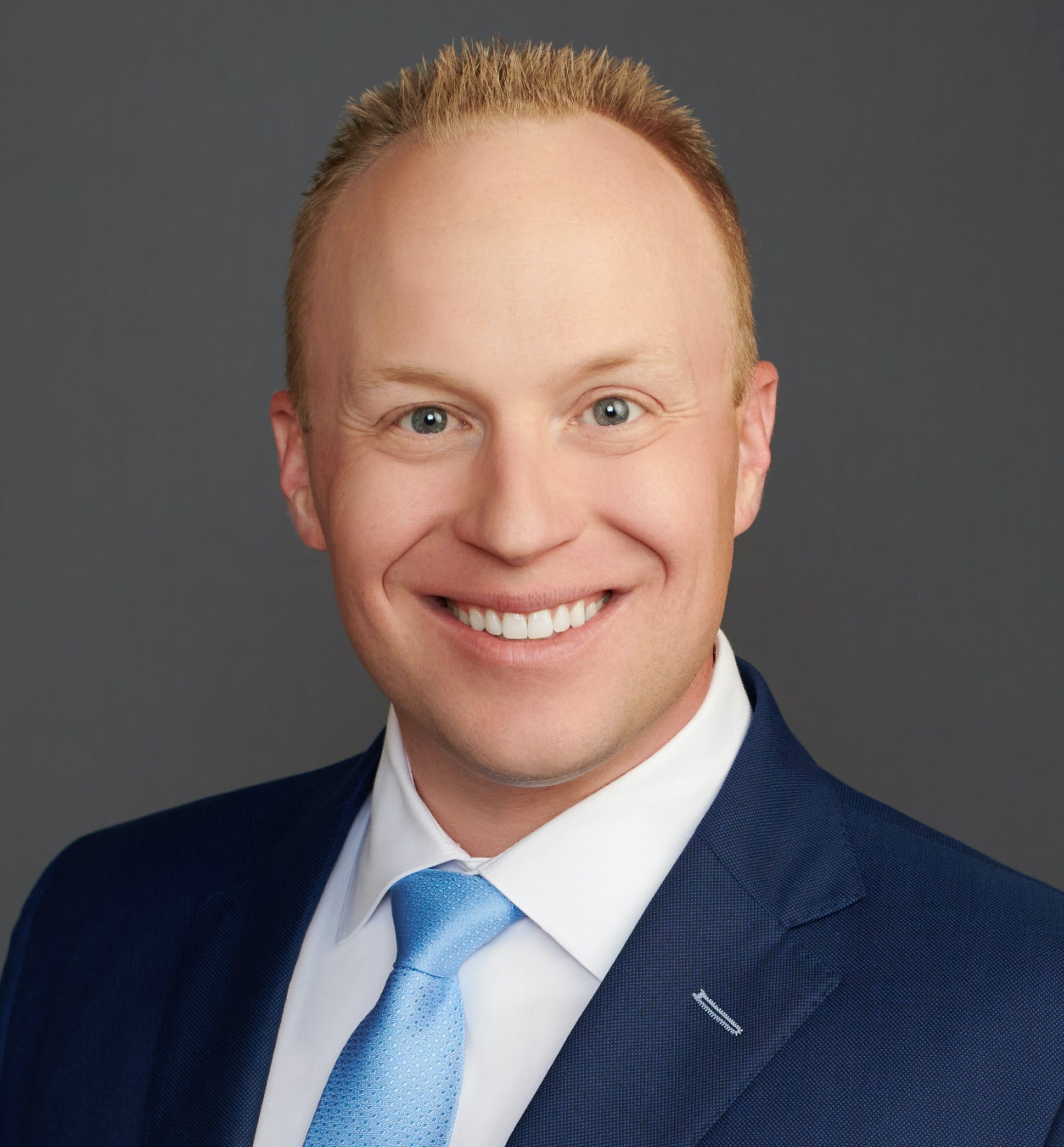 Smiling man in a blue suit and tie against a gray background, identified as James Bogart.